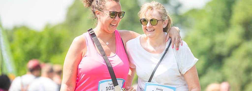Two Race for Life participants. They're smiling and have their arms around each other as they walk.