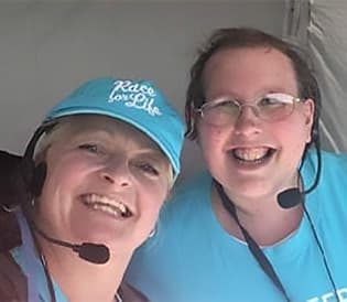 An event volunteer, Lucy, is taking a selfie with a Cancer Research UK staff member in a tent. They're both grinning happily.