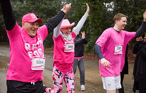 A photo of 3 runners, smiling and wearing pink clothing competing in race for life event.