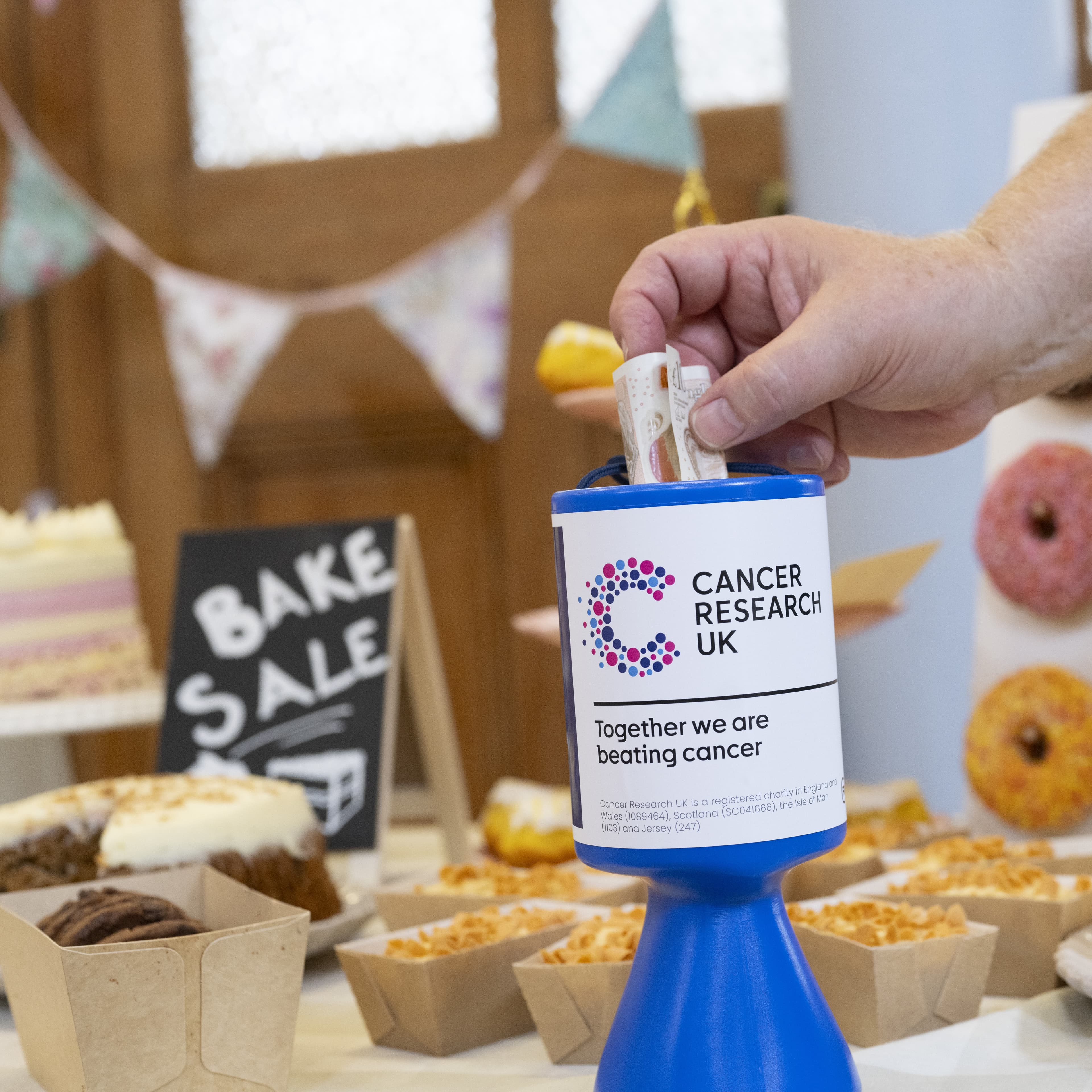 Someone putting money into a collection goblet at a fundraising bake sale.